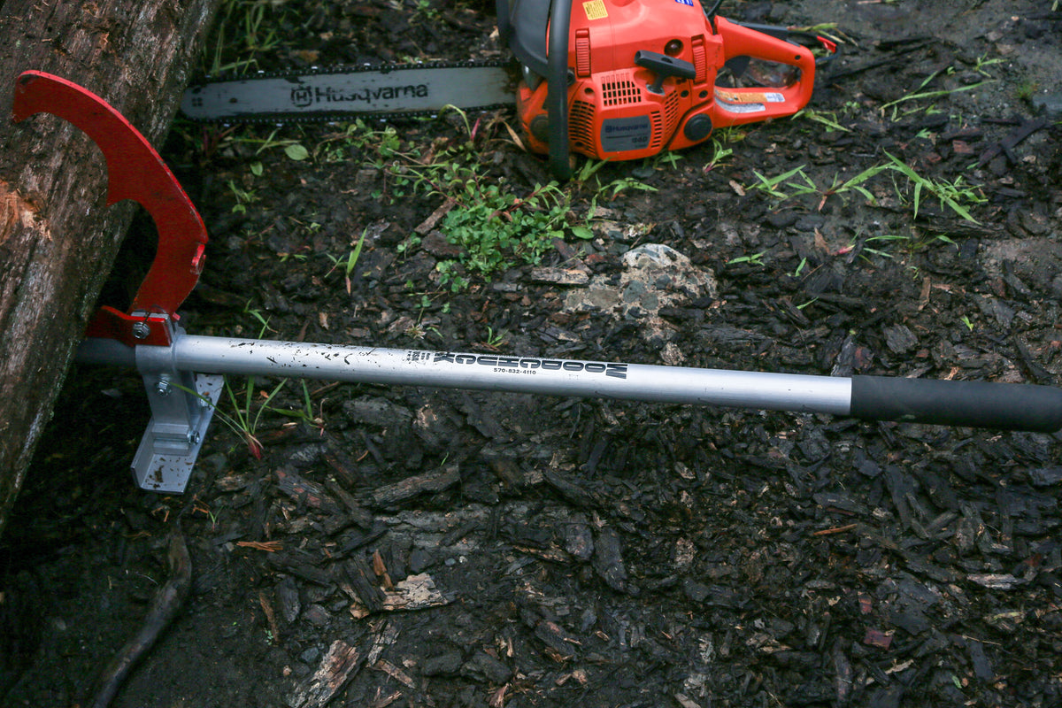 Woodchuck log jack set in the lift position against a log, chainsaw lying on the ground behind it