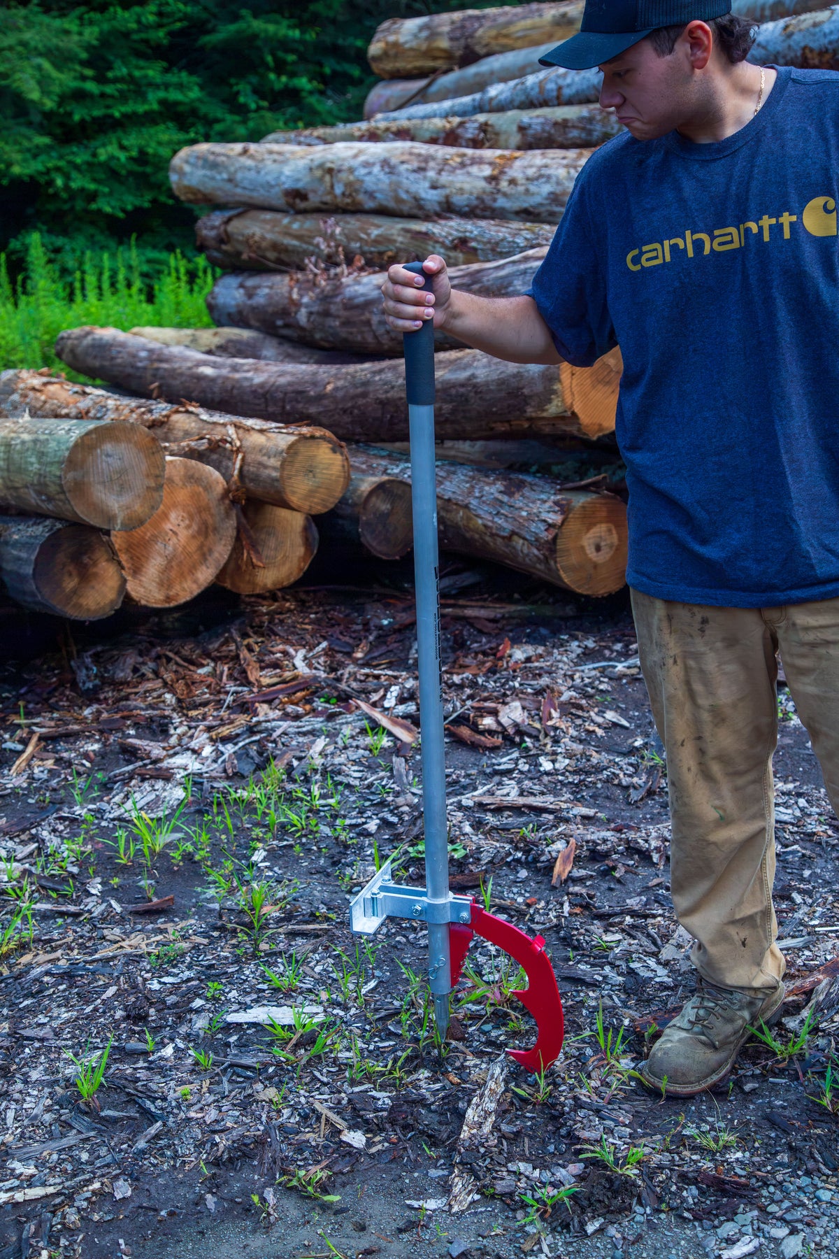 Man holding a Woodchuck DualPro upright with its peavey point in the ground, stacked logs behind him
